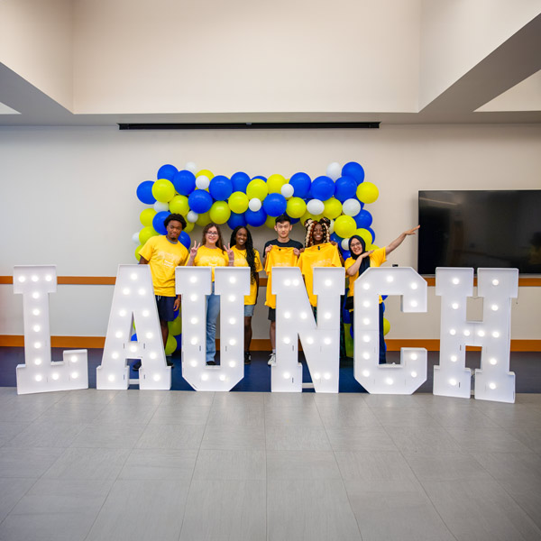 Students posing behind lighted letters that spell LAUNCH